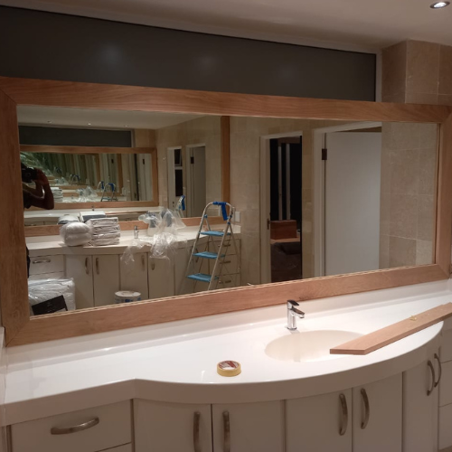 Large custom bathroom mirror with solid timber frame installed above curved vanity